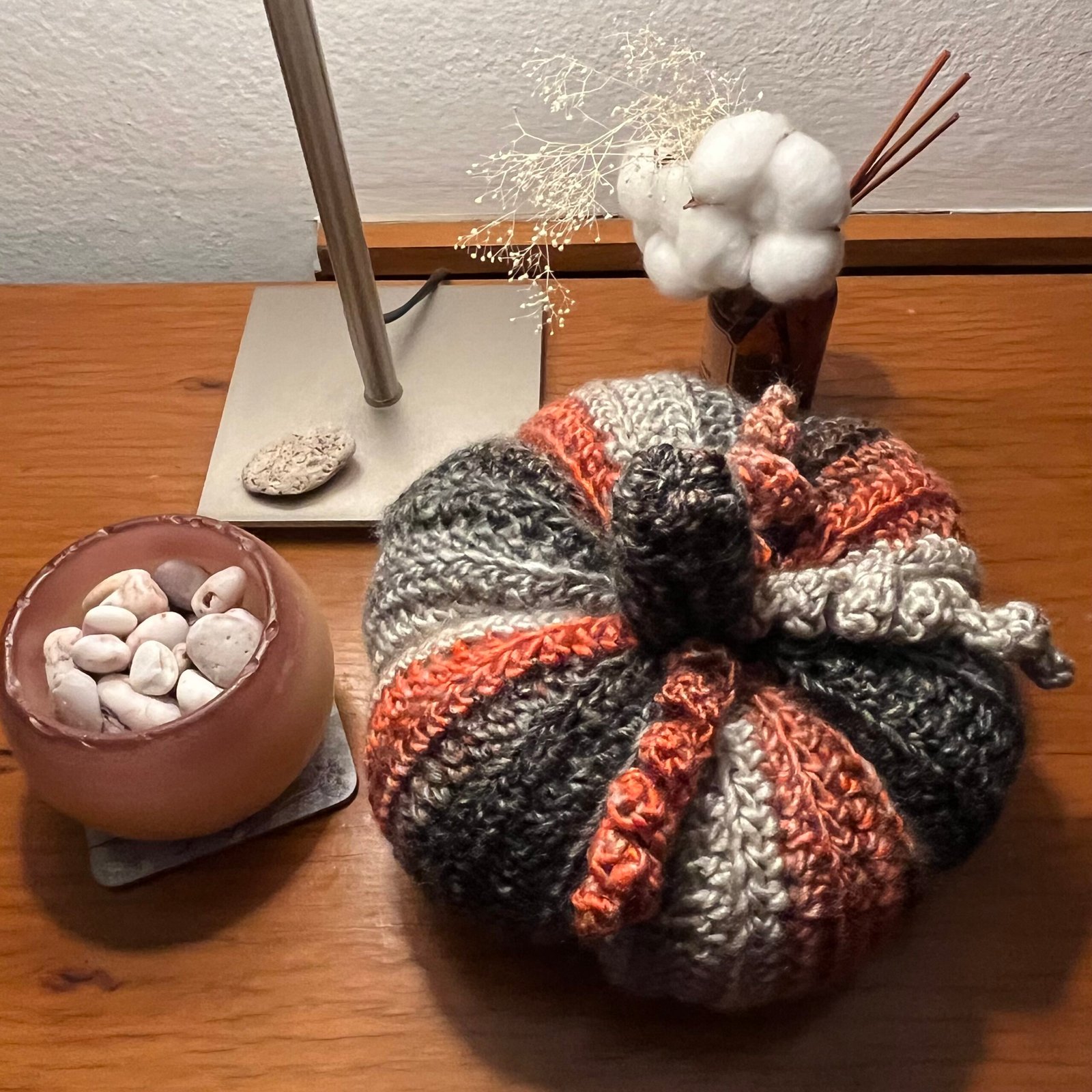 A grey, black and orange crocheted pumpkin on a table with coordinating accessories.