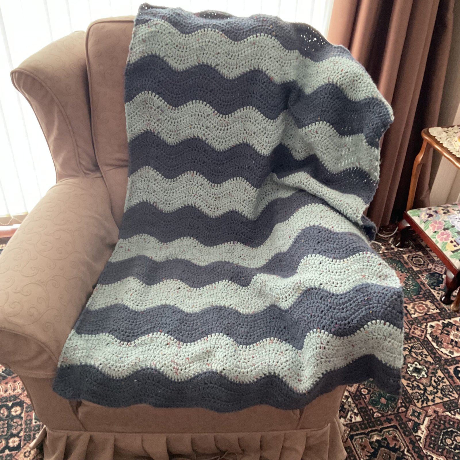 A blue and grey wavy striped crochet blanket on a chair in a living room.
