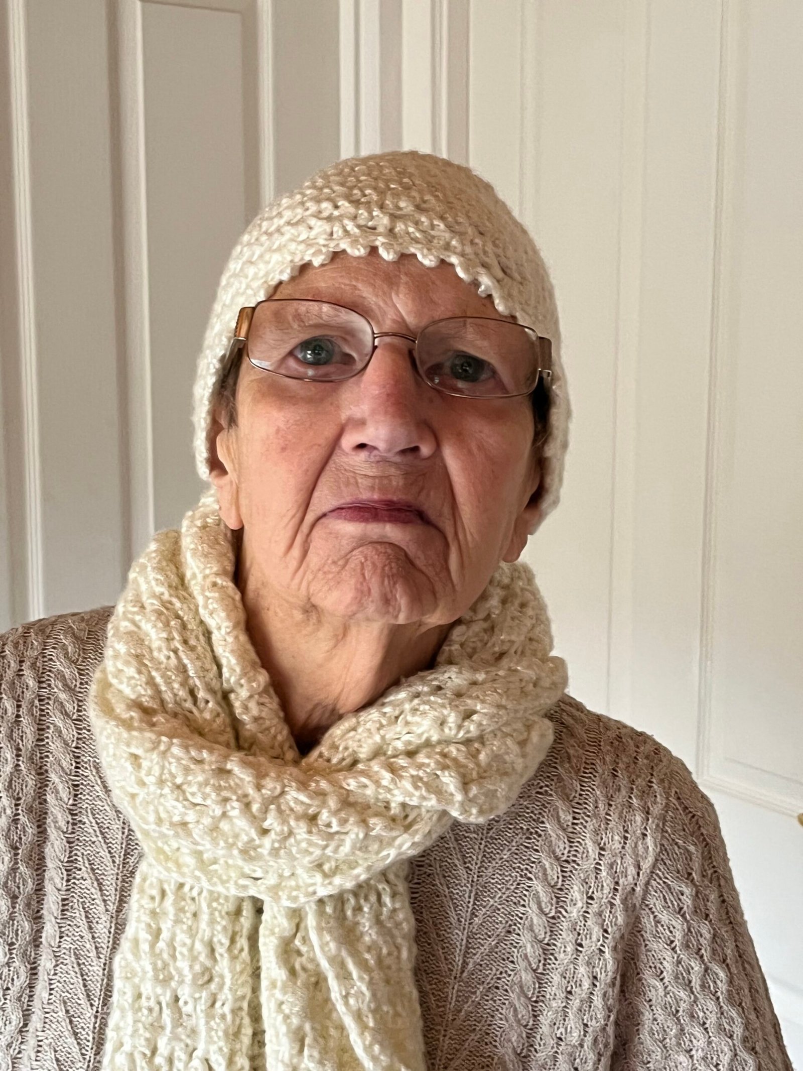 A lady wearing a crocheted cream hat and scarf.